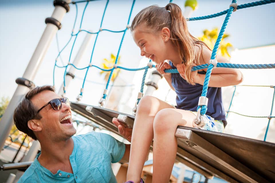 Father and daughter laughing on a boat with blue rope rigging and ocean view