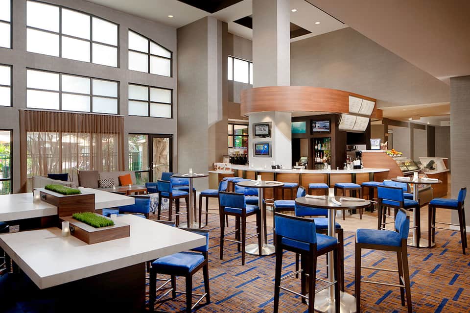Modern hotel lobby with high ceilings, reception desk, blue chairs, and natural light