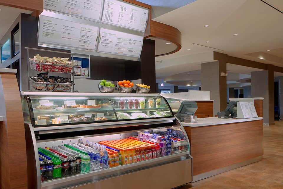 Modern cafe counter with refrigerated display cases, menu boards, fresh fruit, and beverages