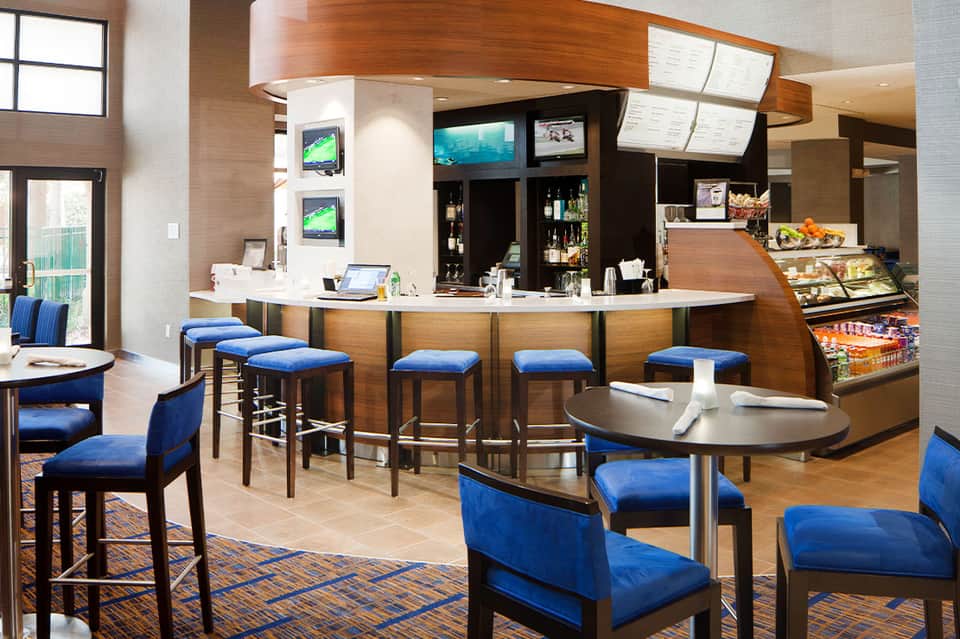 Modern hotel bar and lounge with wooden counter, blue seating, and full-service beverage station