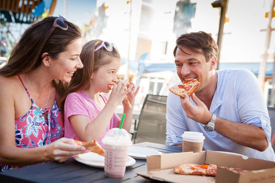 Family of three enjoying pizza together at outdoor beachside dining table with ocean view