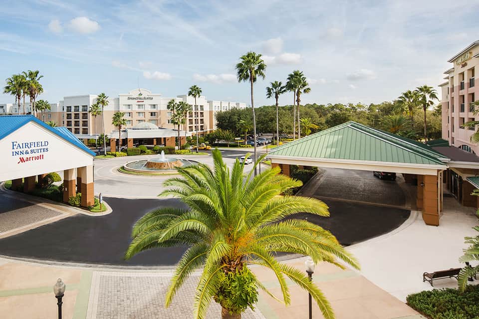 Fairfield Inn & Suites entrance with palm trees, circular fountain, and covered breezeway in Florida setting