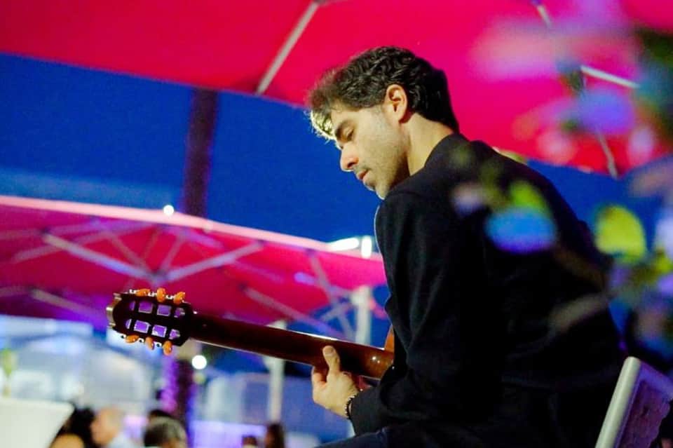 Musician in black shirt playing electric guitar on stage with colorful pink and blue lighting