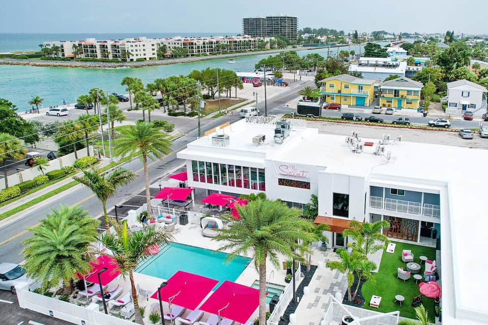 Aerial view of beachfront resort with pink umbrellas, pool, and waterfront buildings