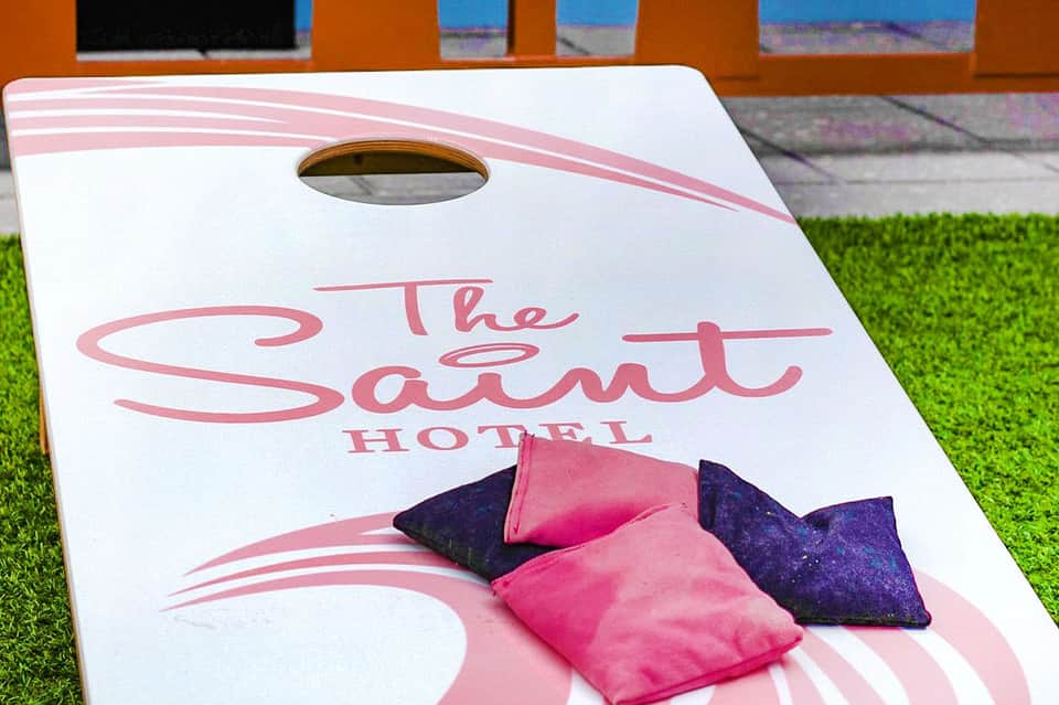 The Salut Hotel cornhole game with pink and navy bean bags on grass