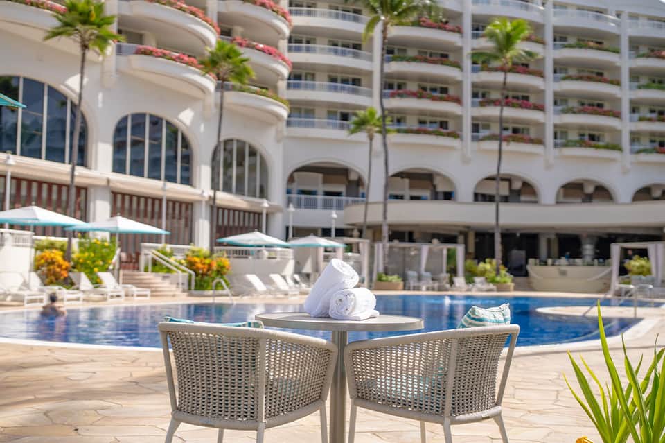 Curved white building with resort pool, lounge chairs, and tropical palm trees