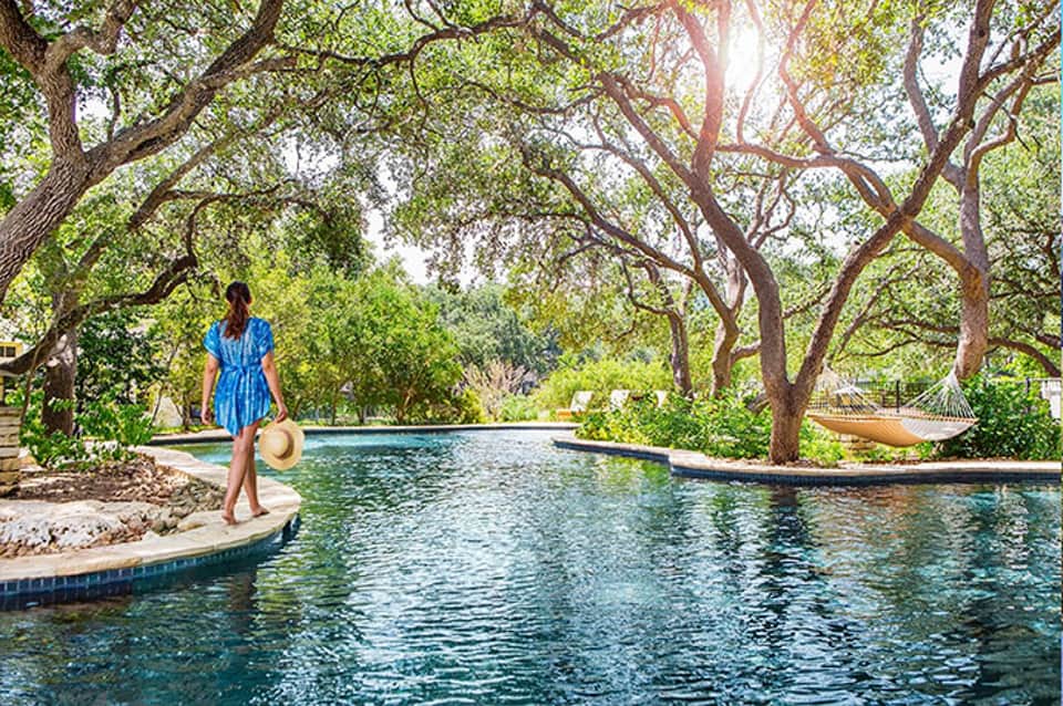 Woman in blue dress standing by tranquil pool surrounded by large oak trees