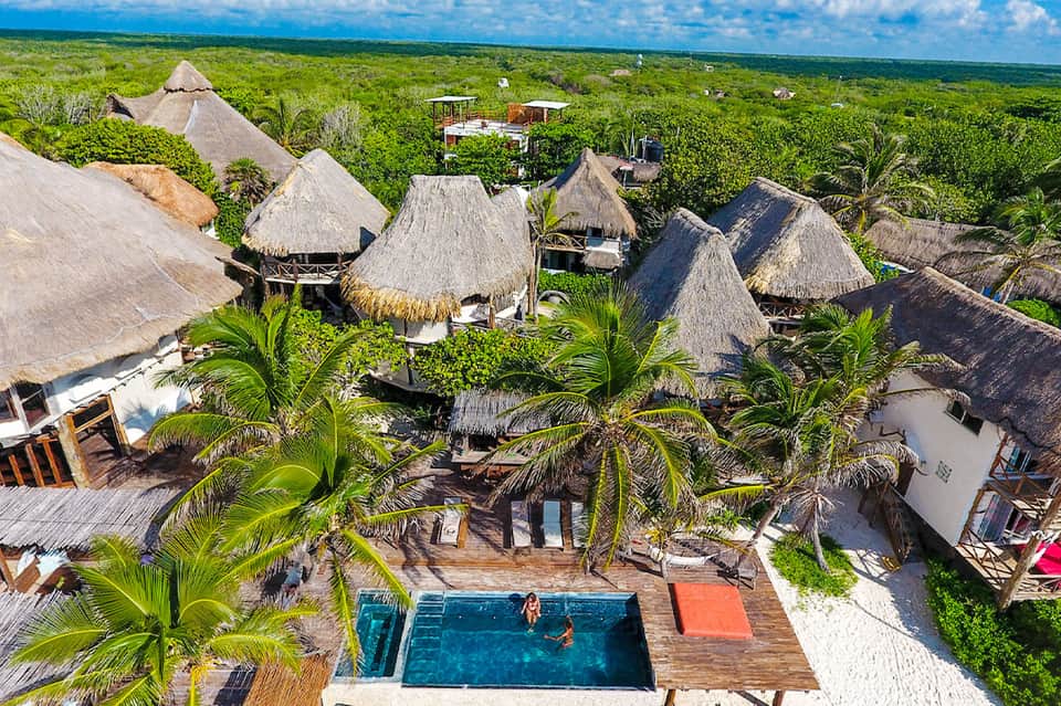Aerial view of tropical jungle resort with thatched-roof bungalows and central pool