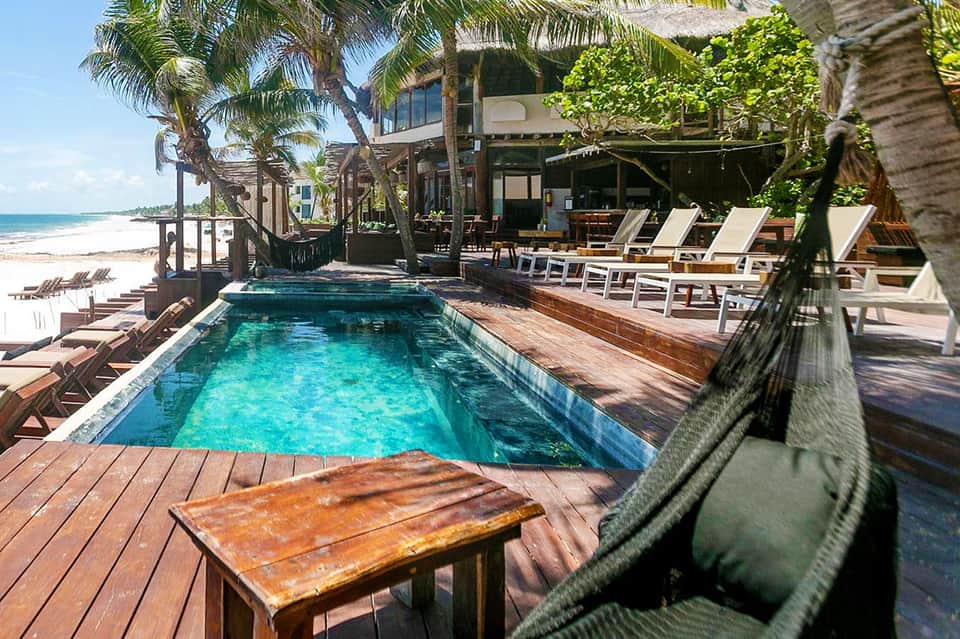 Beachfront infinity pool with turquoise water, wooden deck, palm trees, and ocean view