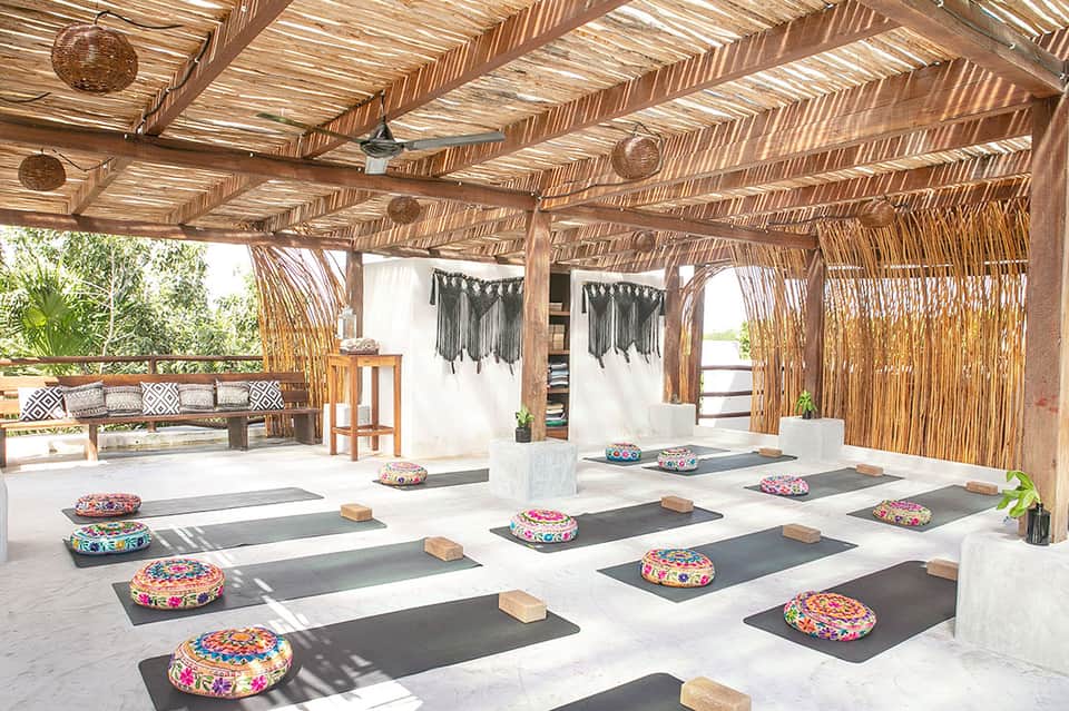 Yoga studio with wooden pergola ceiling, yoga mats with colorful cushions, and natural light