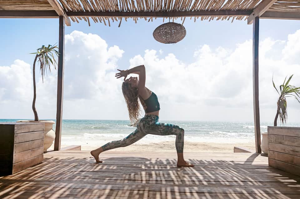 Woman practicing yoga in a beachfront pavilion with ocean view and palm trees