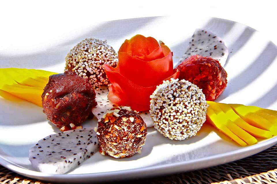 Gourmet dessert plate with chocolate truffles, dragon fruit, yellow mango slices, and white cream sauce under bright sunlight