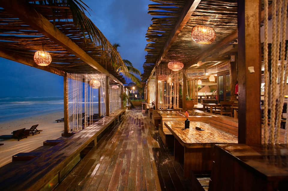 Beachfront wooden boardwalk restaurant with pendant lights and ocean views at dusk