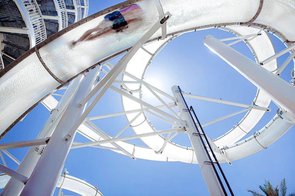 Water slide at resort with person sliding down white tube against blue sky