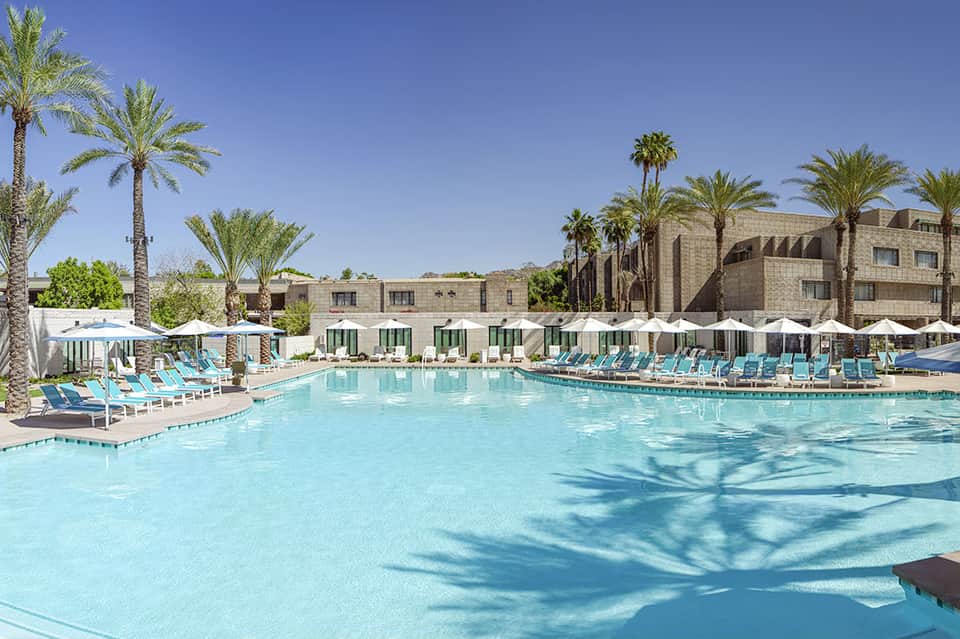 Resort pool with turquoise water, palm trees, and desert mountains