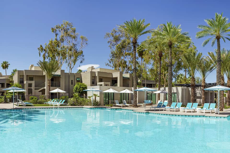 Resort courtyard with turquoise pool, modern concrete buildings, and palm trees
