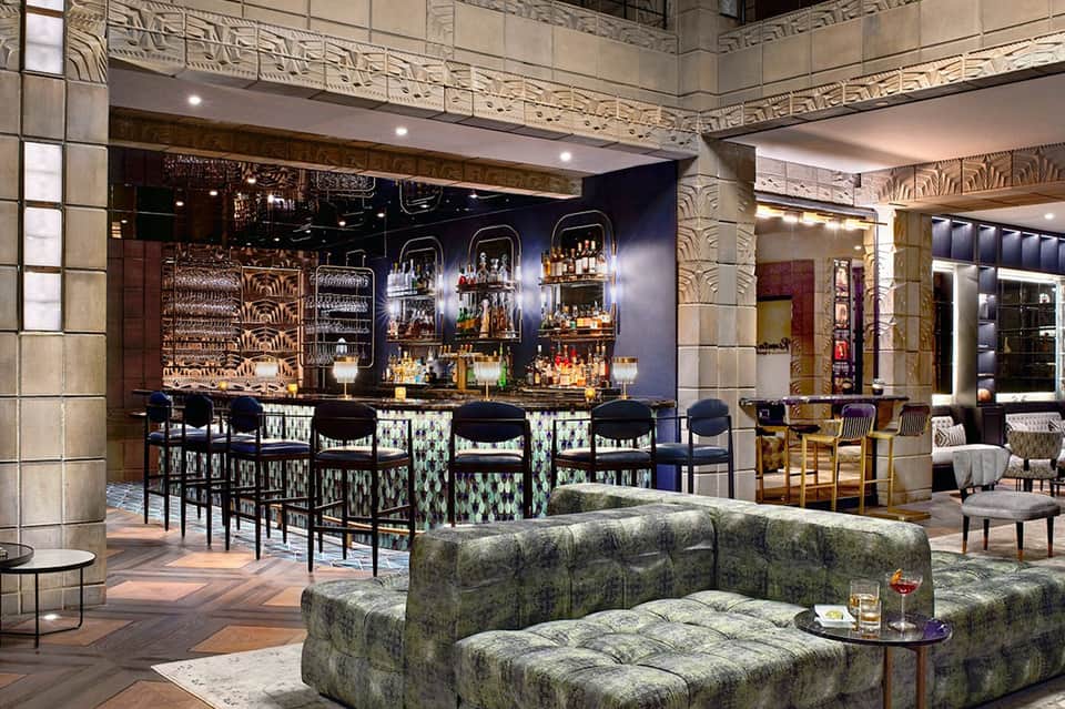 Upscale bar lounge with dark blue walls, ornate ceiling details, and patterned bar seating