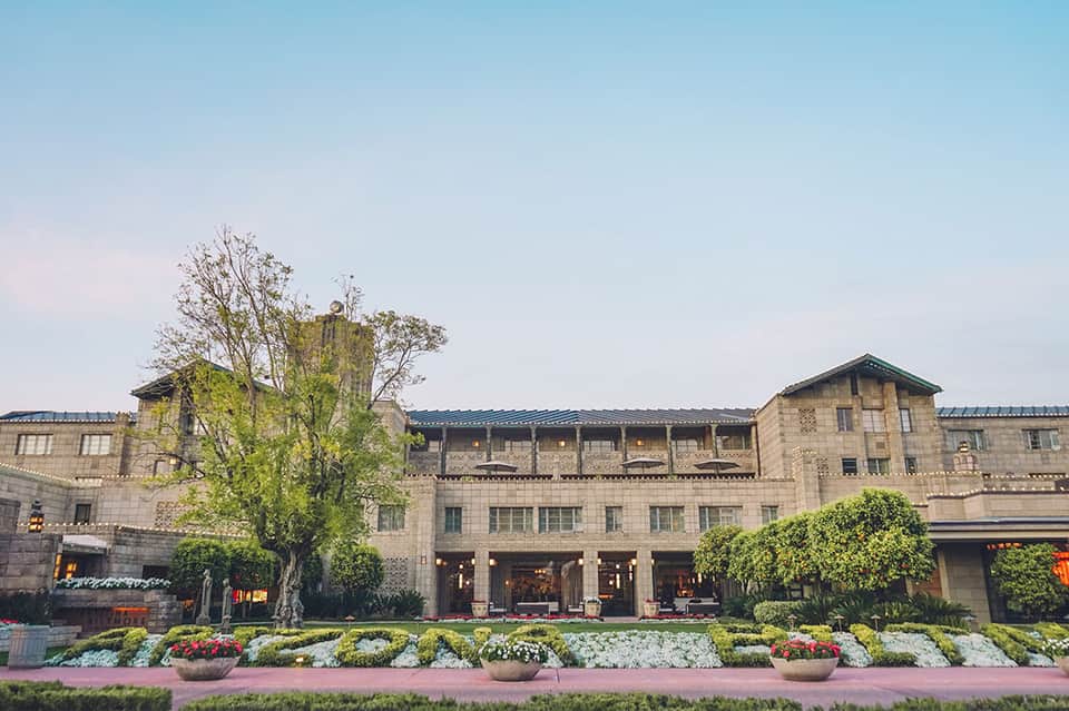 Elegant stone hotel building with manicured gardens and flowering plants along the front entrance
