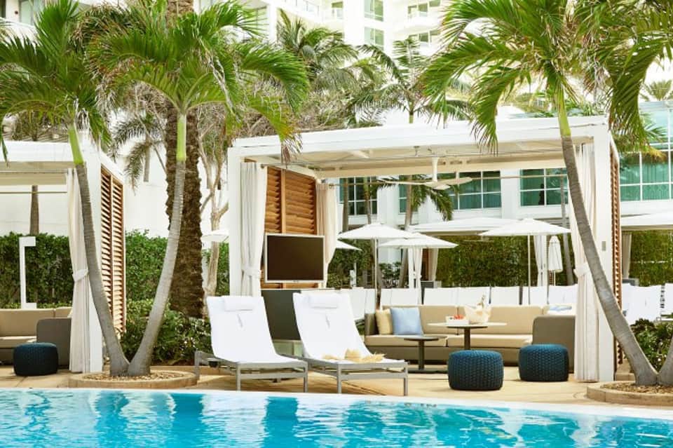 Luxury resort pool area with white cabanas, palm trees, and lounge chairs under pergola shade structures
