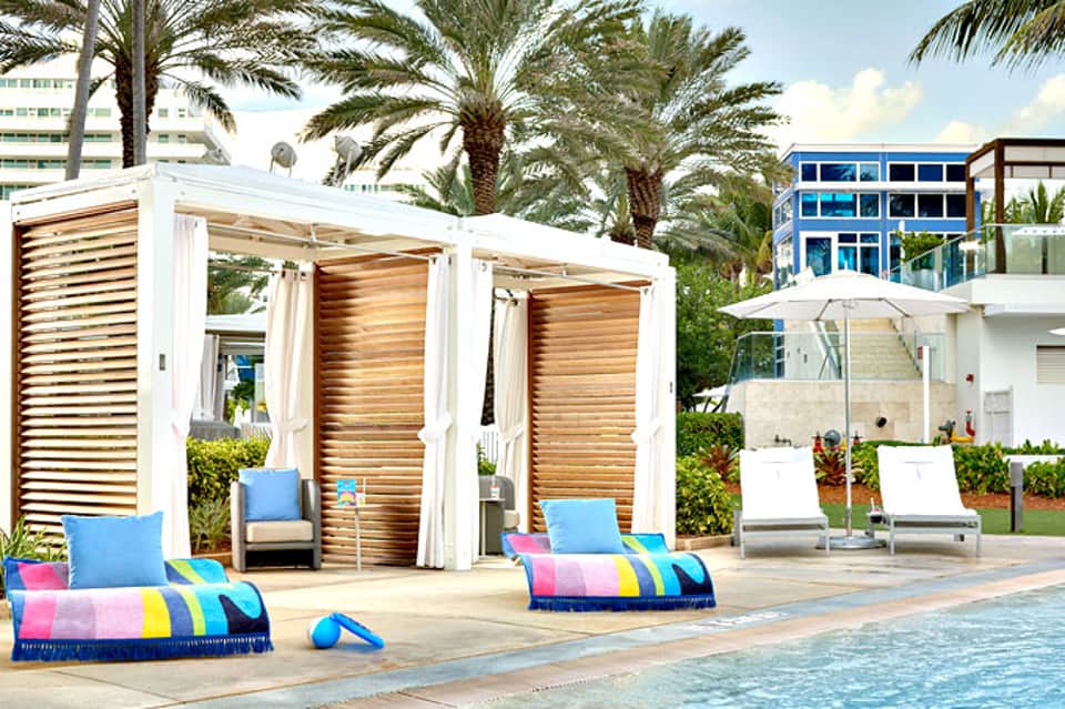 Resort poolside cabanas with colorful striped loungers and palm trees