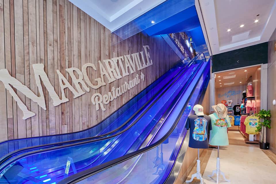 Modern escalators with Margaritaville signage and retail storefront in contemporary indoor mall setting