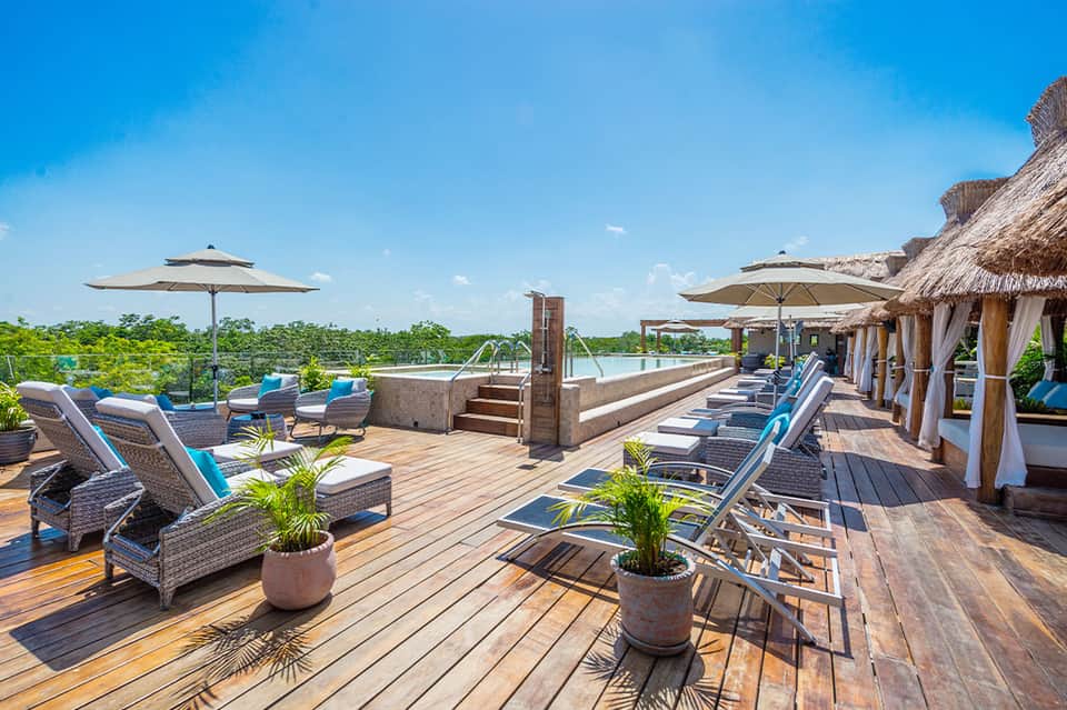 Waterfront resort deck with lounge chairs, umbrellas, and thatched-roof cabanas overlooking landscape