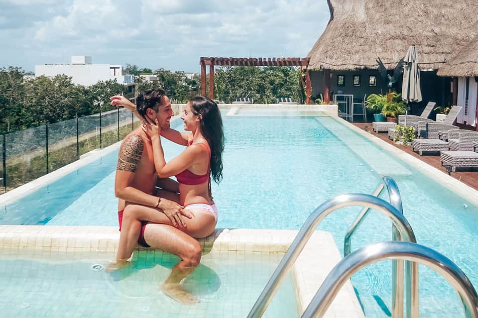 Couple relaxing at the edge of a rooftop infinity pool with city views and thatched cabana