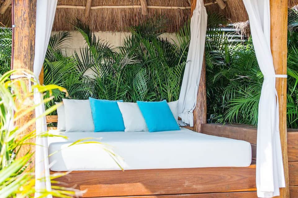 Outdoor cabana bed with white curtains, striped blue pillows, and tropical vegetation