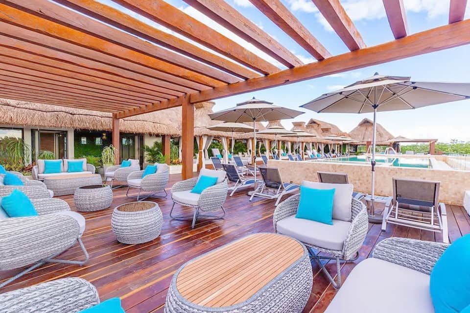 Luxury resort deck with woven lounge chairs, umbrellas, and thatched roof structures
