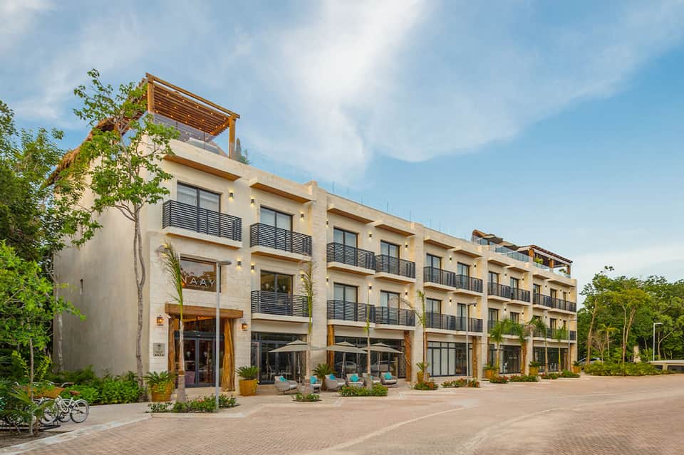 Modern beige residential building with multiple balconies, ground-floor retail spaces, and landscaped courtyard with seating areas
