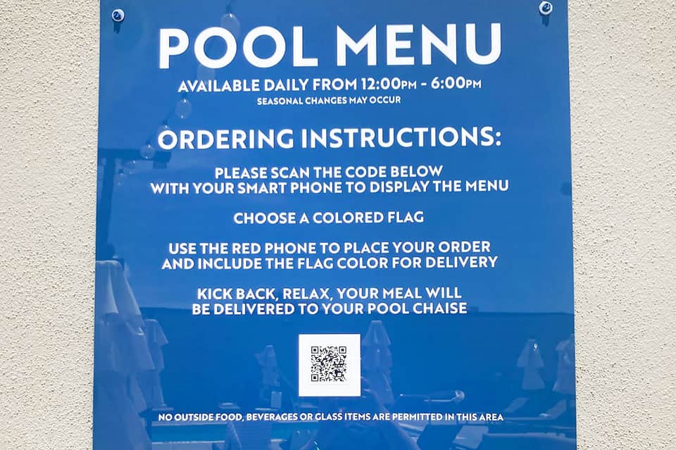Blue sign with pool menu ordering instructions, QR code, and service details posted on concrete wall