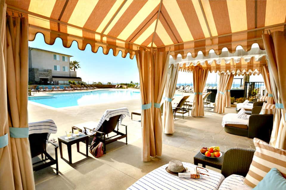 Covered poolside cabanas with striped awnings and lounge chairs overlooking the pool area