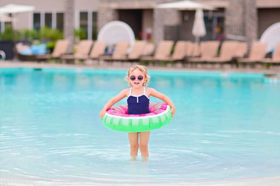 Young child in colorful swim ring standing in shallow resort pool wearing sunglasses
