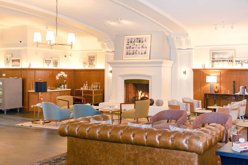 Elegant hotel lobby with leather sofa, fireplace, wood paneling, and classic furnishings