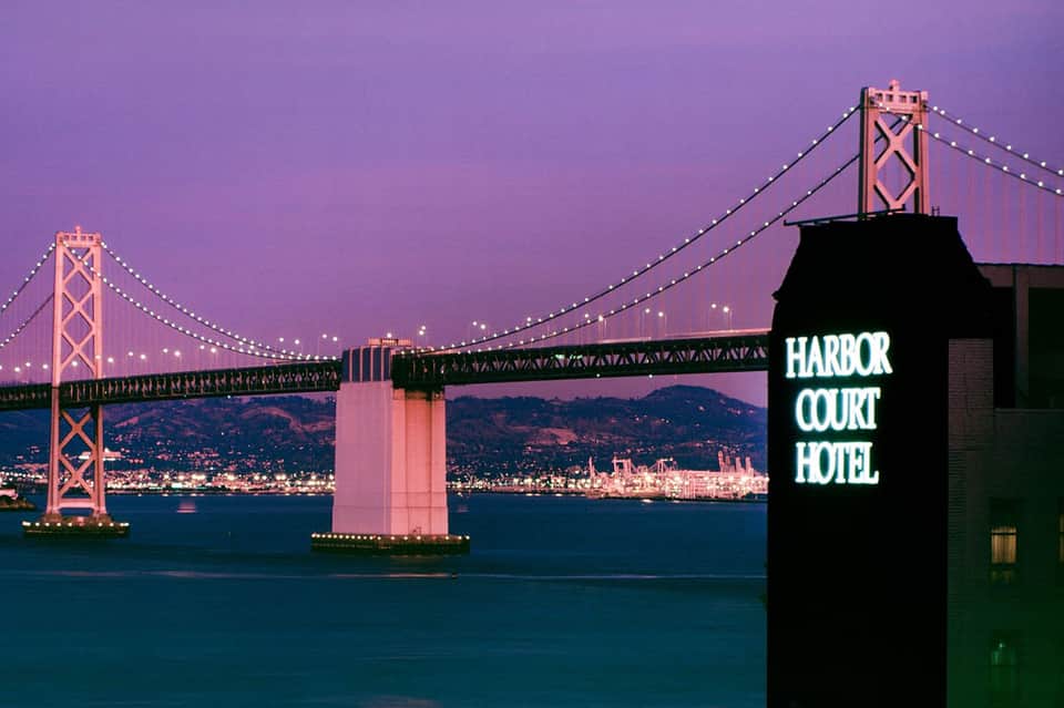 Bay Bridge illuminated at dusk with Harbor Court Hotel sign in foreground