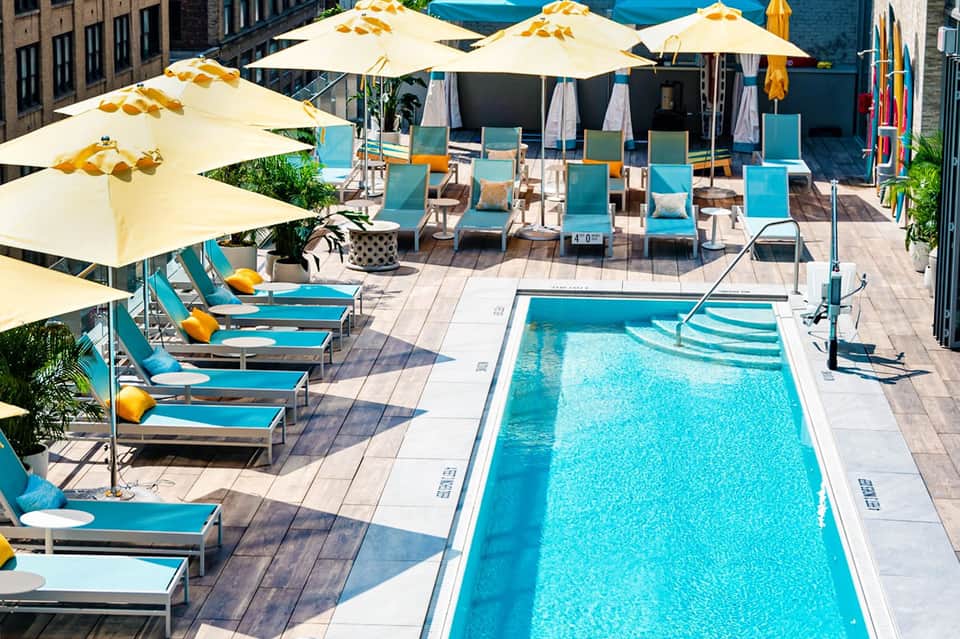 Rooftop pool deck with turquoise loungers, cream umbrellas, and city skyline