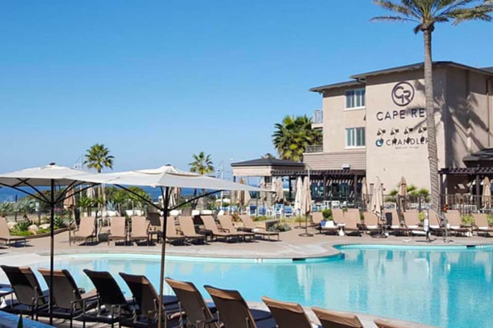 Cape Rey resort pool area with turquoise water, lounge chairs, umbrellas, and palm trees under clear blue sky