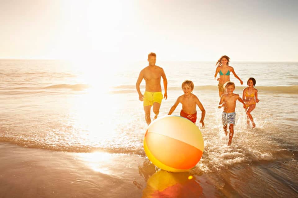 Family playing with a yellow beach ball in the ocean at sunset