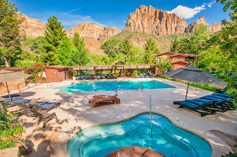 Resort pool with spa tub nestled among red rock formations and pine trees with lounge chairs