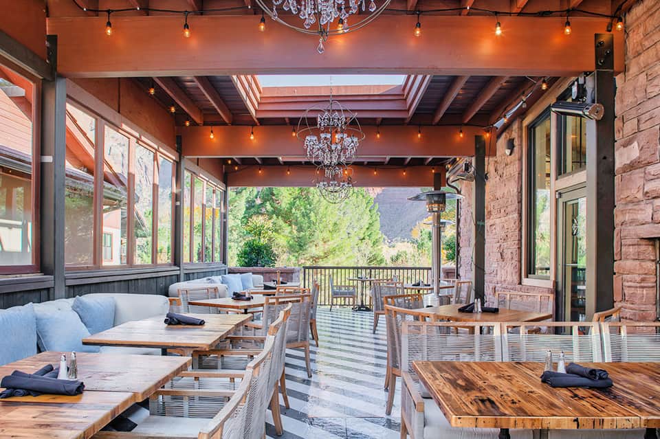 Modern covered dining patio with wooden tables, chairs, and mountain valley views through large windows