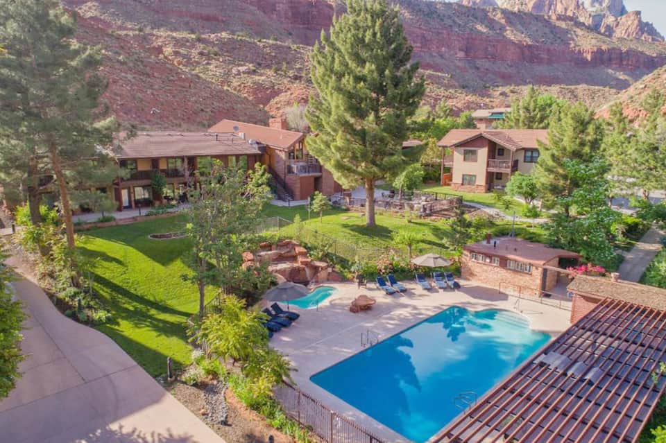 Desert resort nestled among red canyon cliffs with adobe-style buildings, pools, and green landscaping
