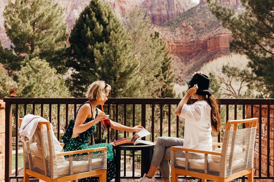 Two women relaxing on a deck overlooking the Grand Canyon with pine trees and canyon views