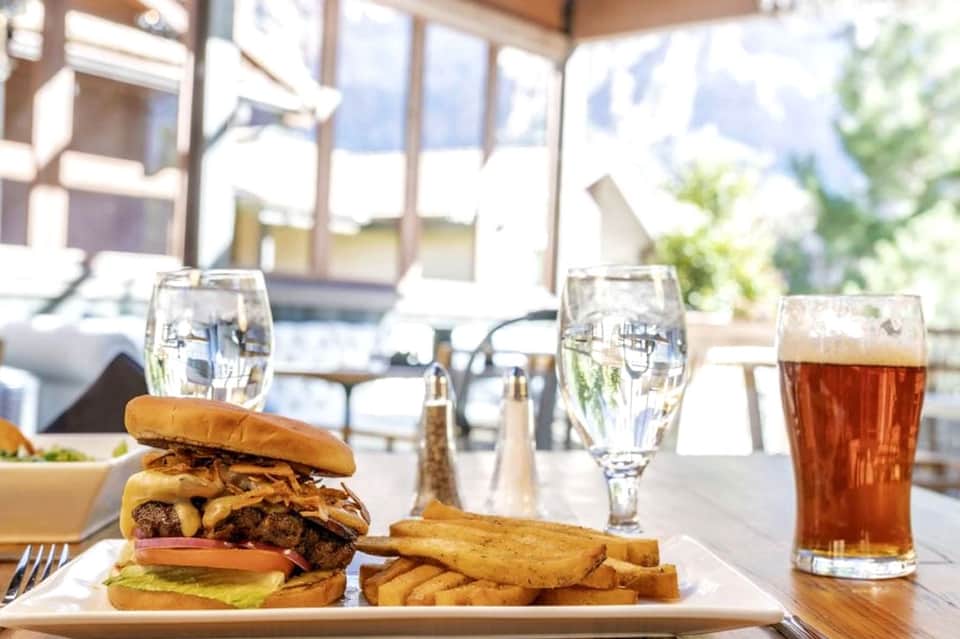 Gourmet burger and fries served on a patio with mountain views and beverages