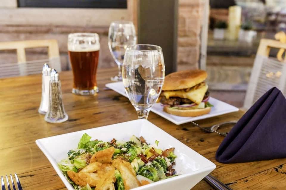 Fine dining table with salad, burger, beer, and water glasses on wooden surface