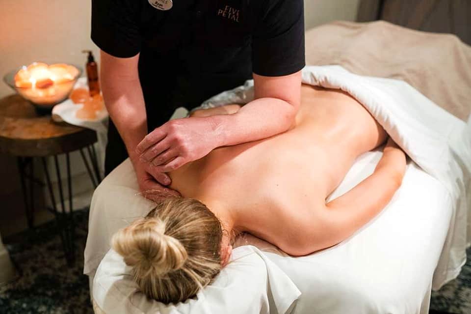 Spa therapist performing back massage on client in relaxation room with candles and soft lighting