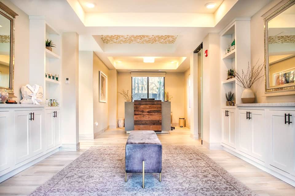 Spa interior hallway with white cabinetry, mirrors, wooden accent wall, and modern lighting