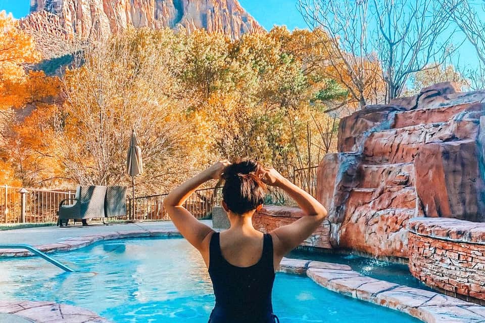 Woman in pool at mountain resort with red rock formations and autumn foliage backdrop