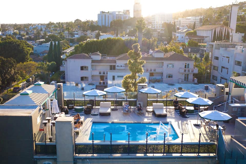 Resort rooftop pool with blue umbrellas overlooking hillside neighborhood during golden hour