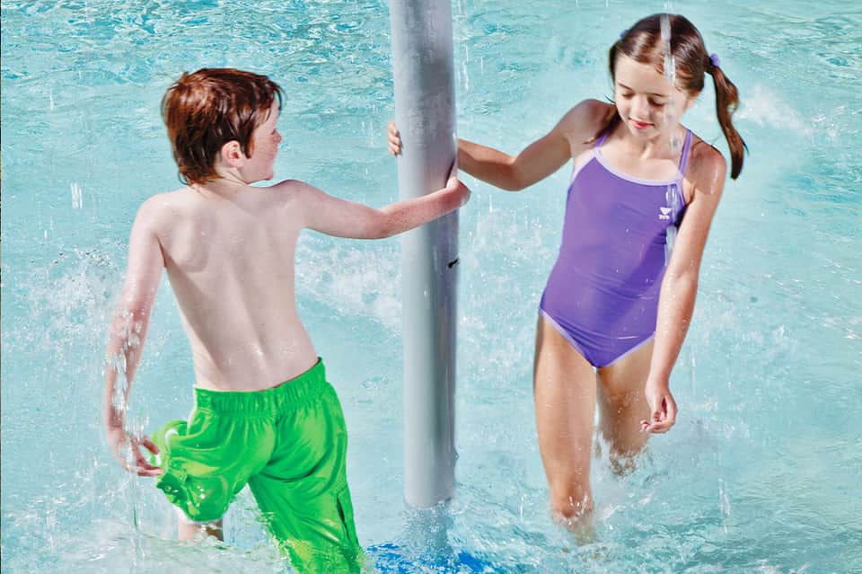 Two children playing in shallow turquoise pool water around support column