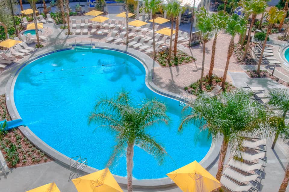 Aerial view of kidney-shaped pool surrounded by palm trees, lounge chairs, and yellow umbrellas